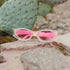 A pair of pink-frame sunglasses with clear lenses and rhinestone embellishments on the lenses.