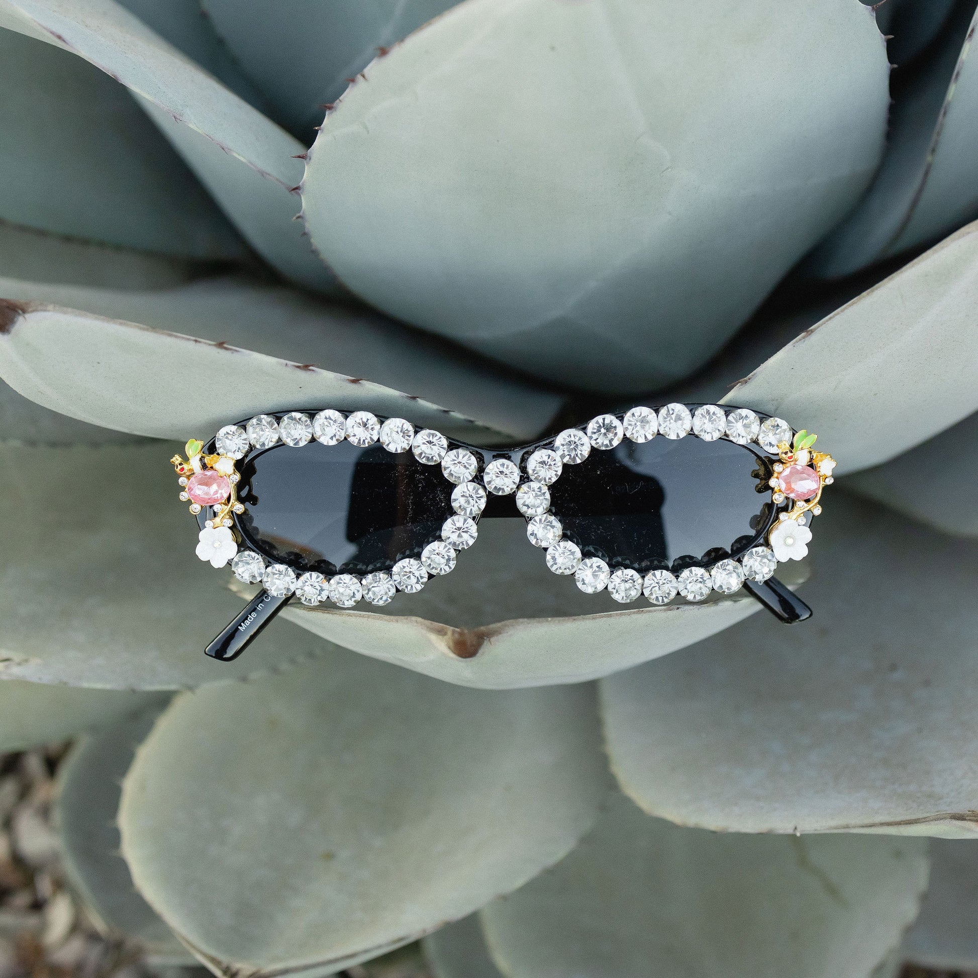 Women's sunglasses with a black frame, decorated with crystal rhinestones and pink flower embellishments.