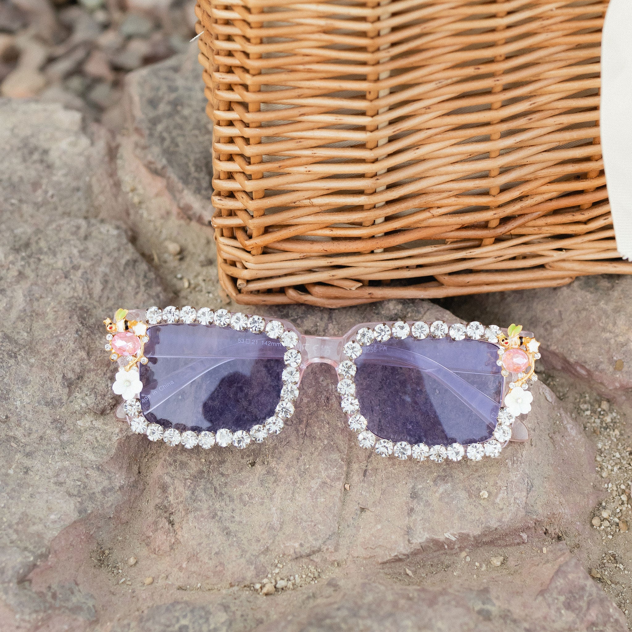 A pair of rectangular sunglasses with crystal rhinestones on the frames and flower jewelry details on the sides.