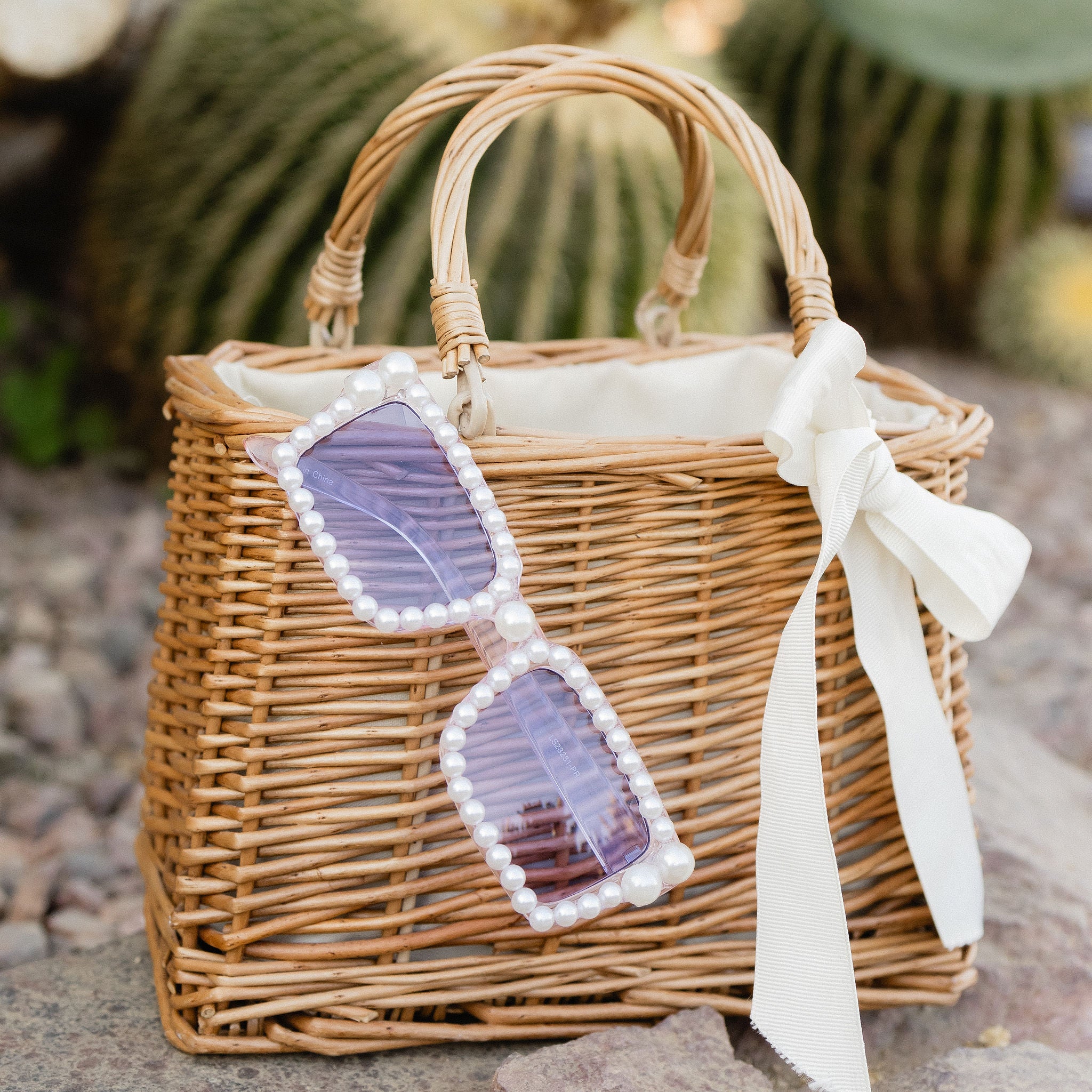 A pair of rectangle women's sunglasses with white pearls along the frame, lavender lenses.